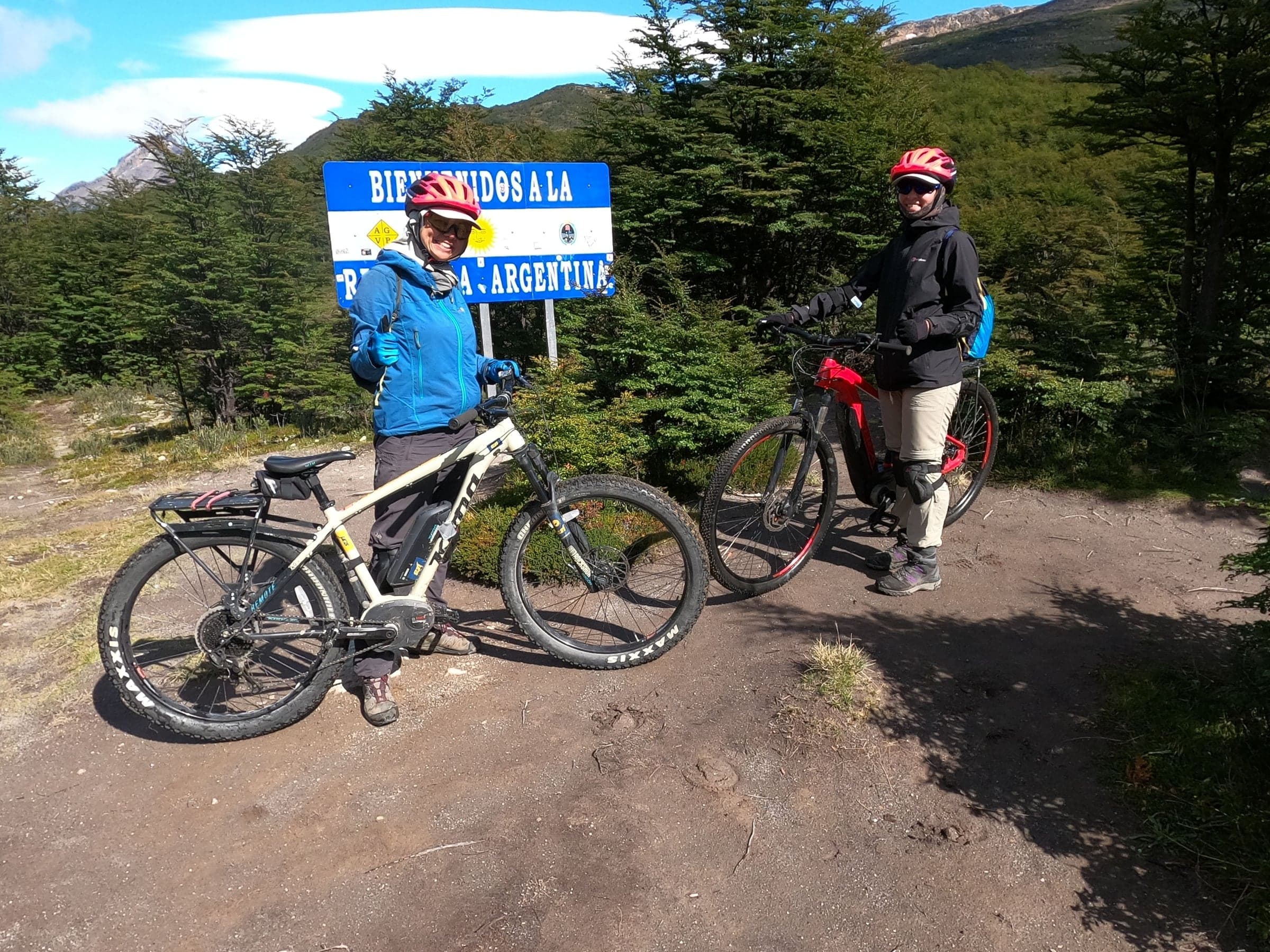Due viaggiatori con le loro e-bike accanto al cartello di benvenuto in Argentina, al cippo di confine