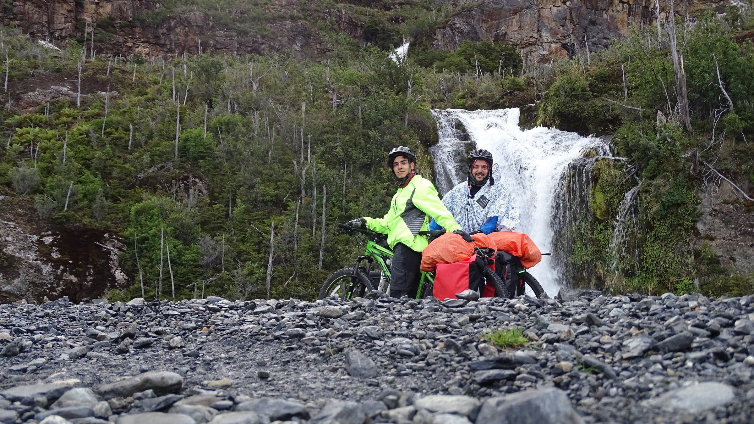 Javi e Nacho con le bici cariche davanti a una cascata, durante la traversata del 2018