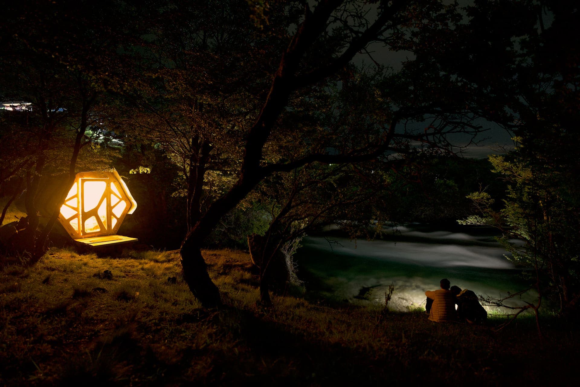 Un micro-rifugio illuminato dall'interno, di notte, accanto al Río Cochrane