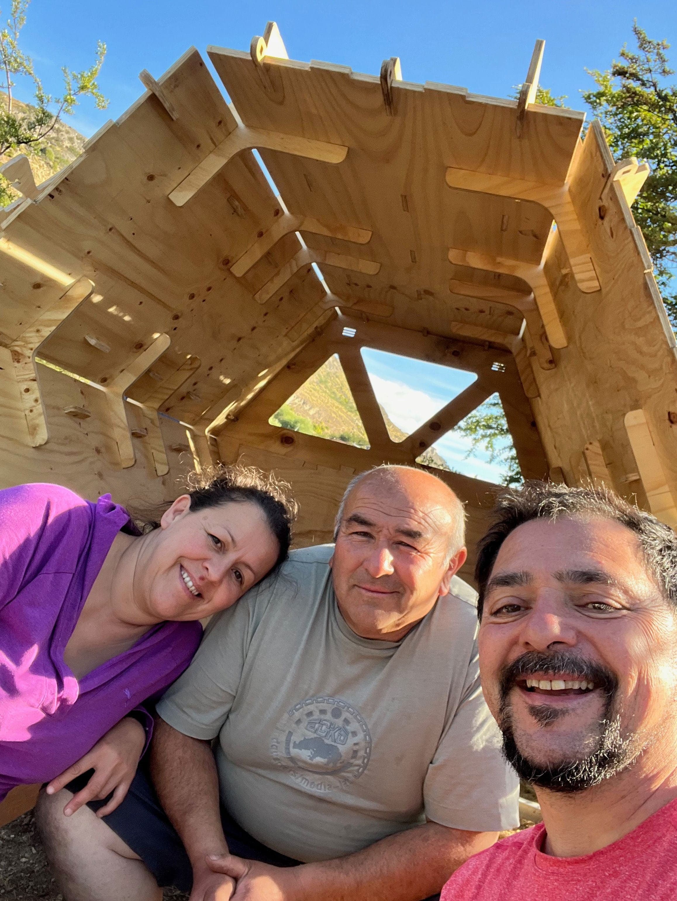 Tre persone sorridono dentro un micro-rifugio di legno