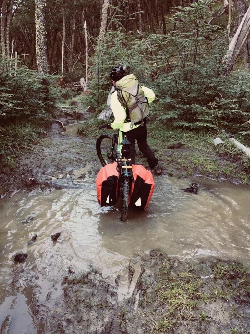 Un ciclista spinge la sua bicicletta carica lungo un sentiero fangoso nel bosco
