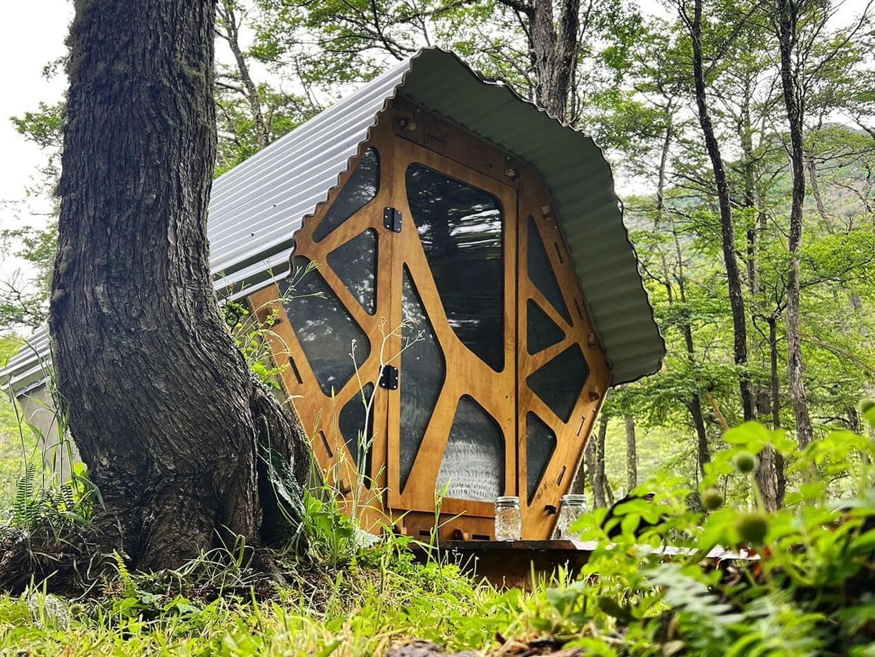 Un micro-rifugio di legno tra gli alberi del bosco, con la luce del pomeriggio