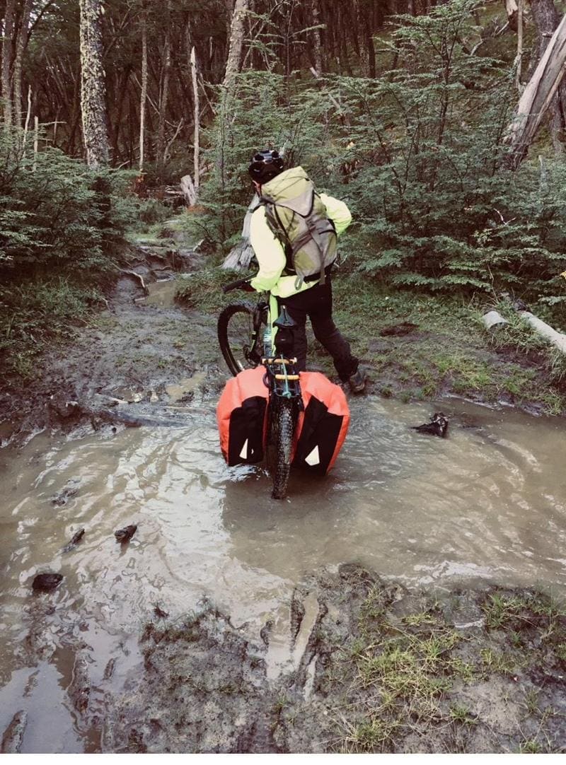 Un ciclista empuja su bicicleta cargada por un sendero embarrado en el bosque