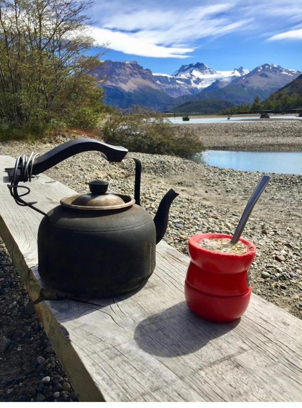 Una tetera negra y un mate rojo sobre una mesa de madera, frente al lago y la cordillera