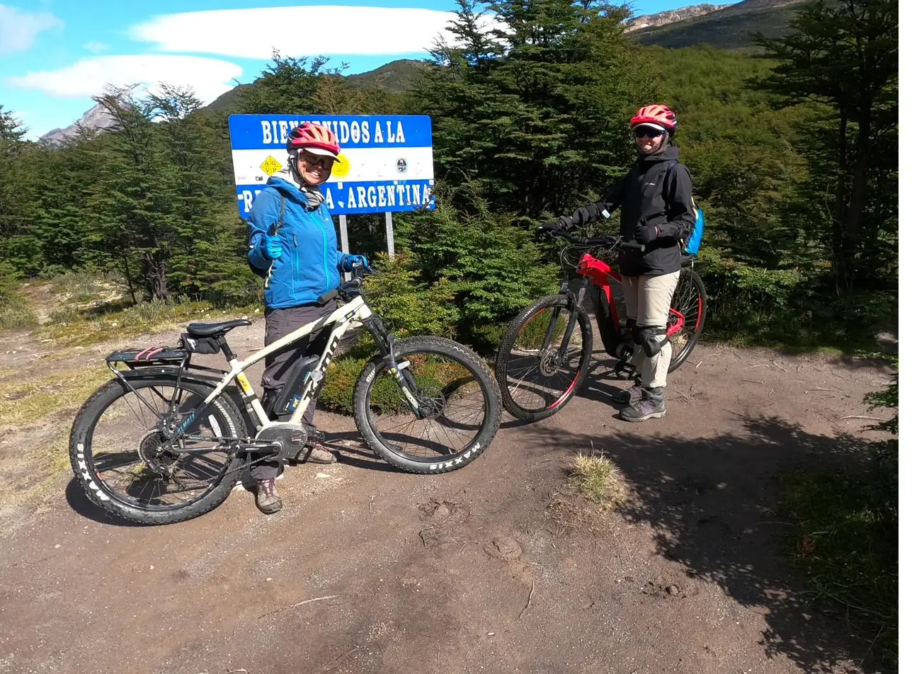 Dos ciclistas con sus e-bikes junto al cartel de bienvenida a la Argentina en el hito fronterizo